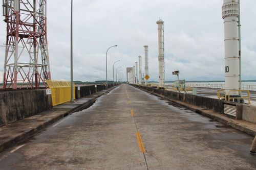 Free A deserted industrial walkway with towering structures on one side and cloudy sky. Stock Photo