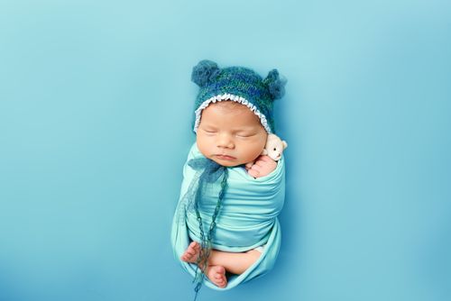 Free Adorable newborn baby wrapped in blue with a bear hat, peacefully sleeping. Stock Photo