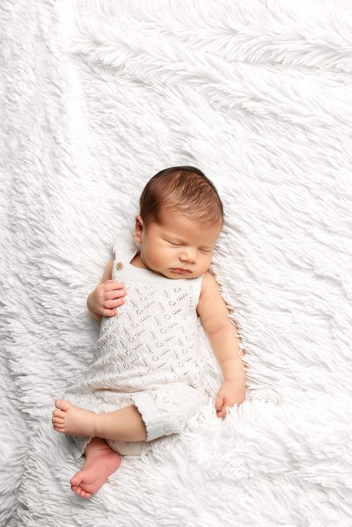 Free A peaceful newborn baby in cozy knitted outfit sleeping on a fluffy white blanket. Stock Photo