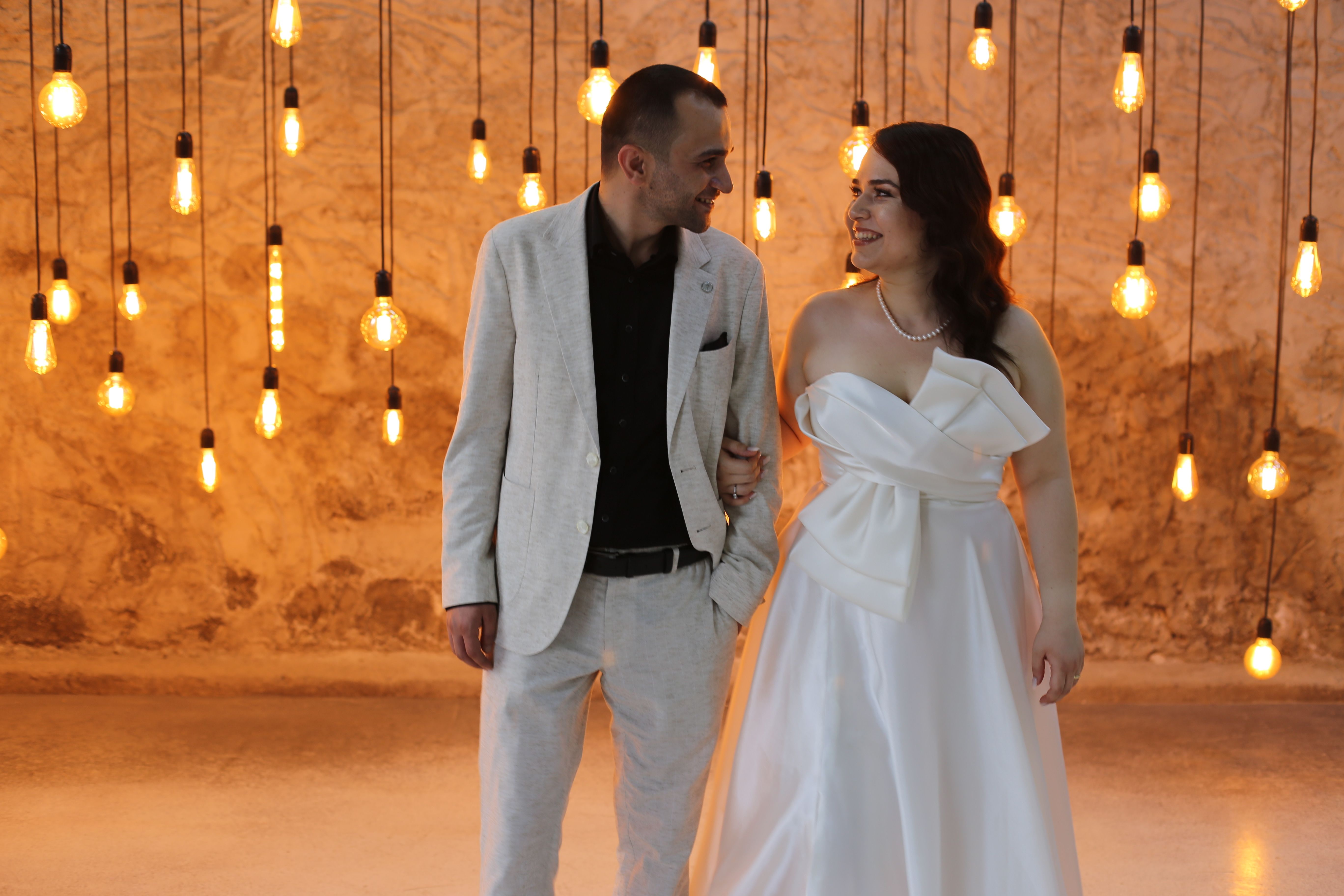 Couple in elegant attire, surrounded by warm hanging lights, embracing joy. - Photo by İSMAİL TEMİZTÜRK on Pexels