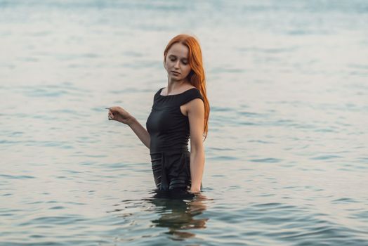 Woman in black dress standing in calm sea water, serene atmosphere.