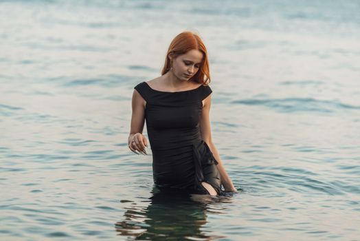 Young woman in black dress standing in sea, exuding peace and contemplation.