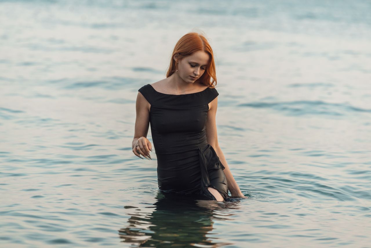 young woman in black dress standing in sea exuding peace and contempla