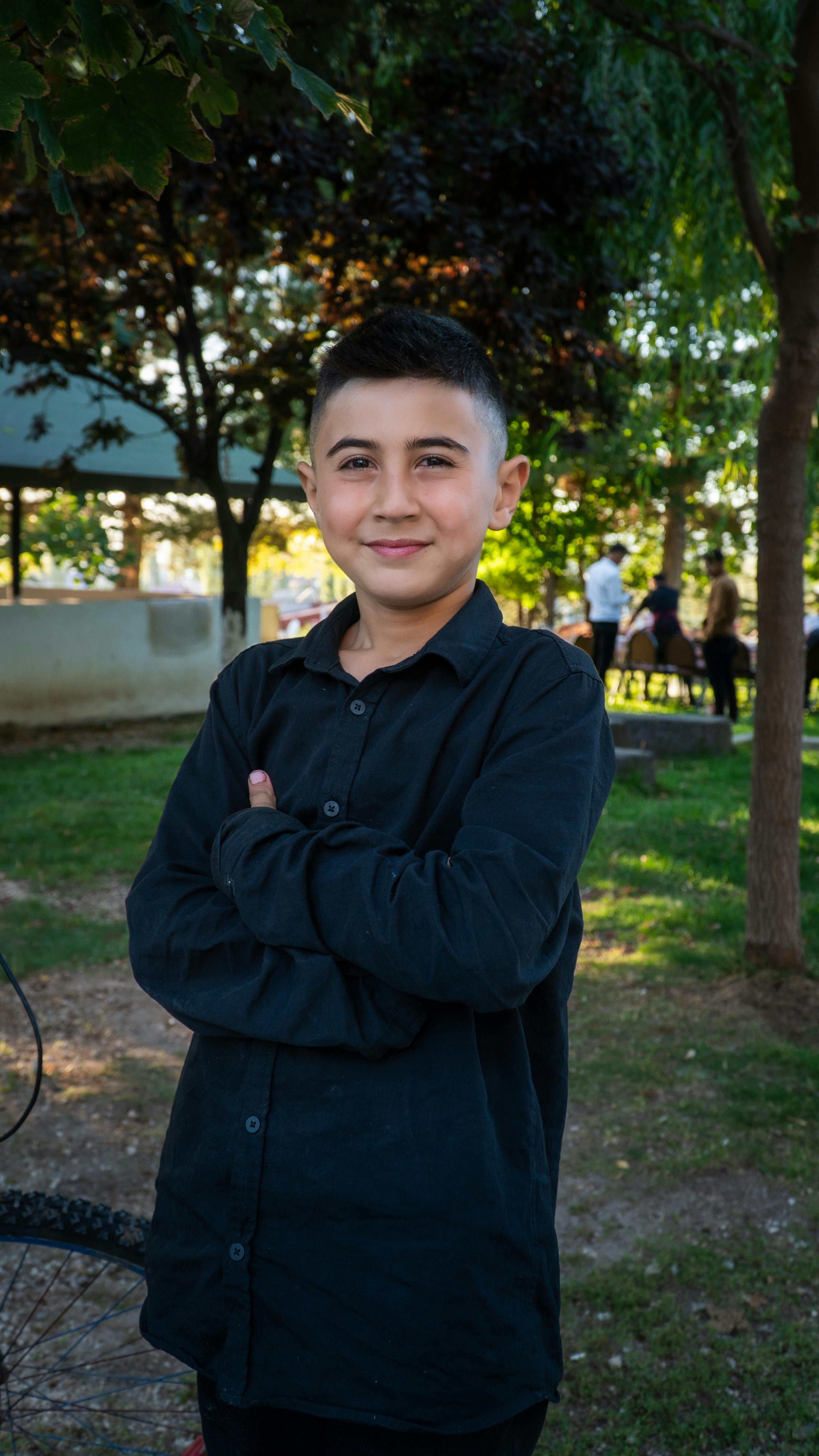 Charming portrait of a young boy smiling in a lush park setting in Niğde, Türkiye.