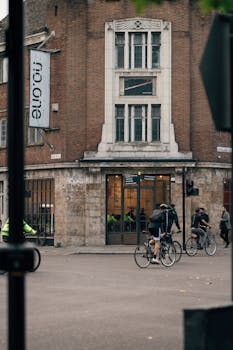 Cyclists pass by a historic building in London, England on a typical day, showcasing urban life.