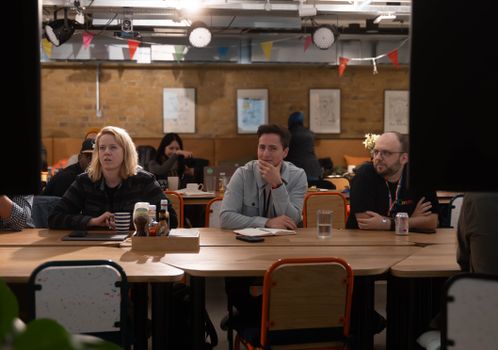 Group of professionals attentively listening during an indoor business meeting with coffee and laptops.