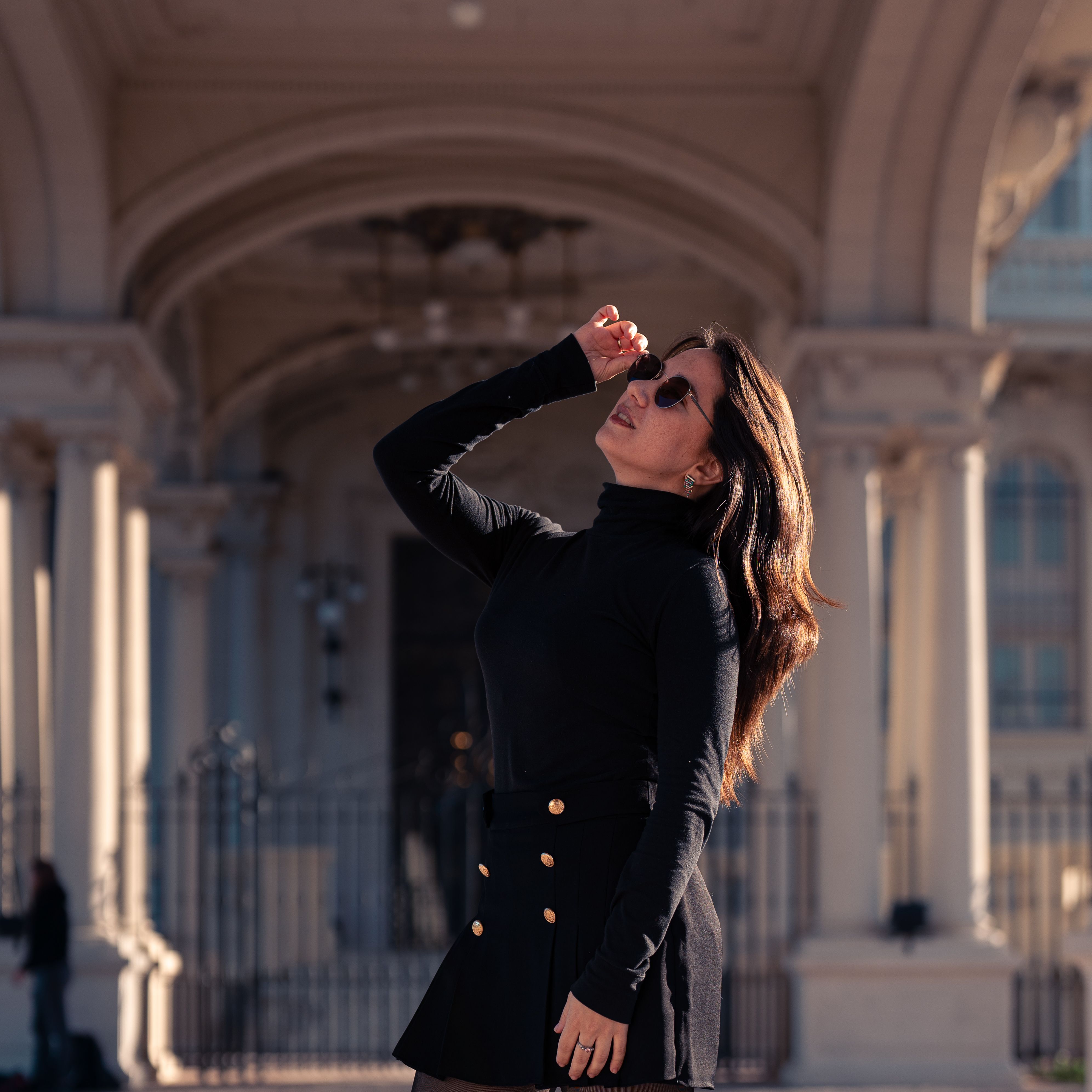Confident woman in urban architecture wearing sunglasses, black attire.