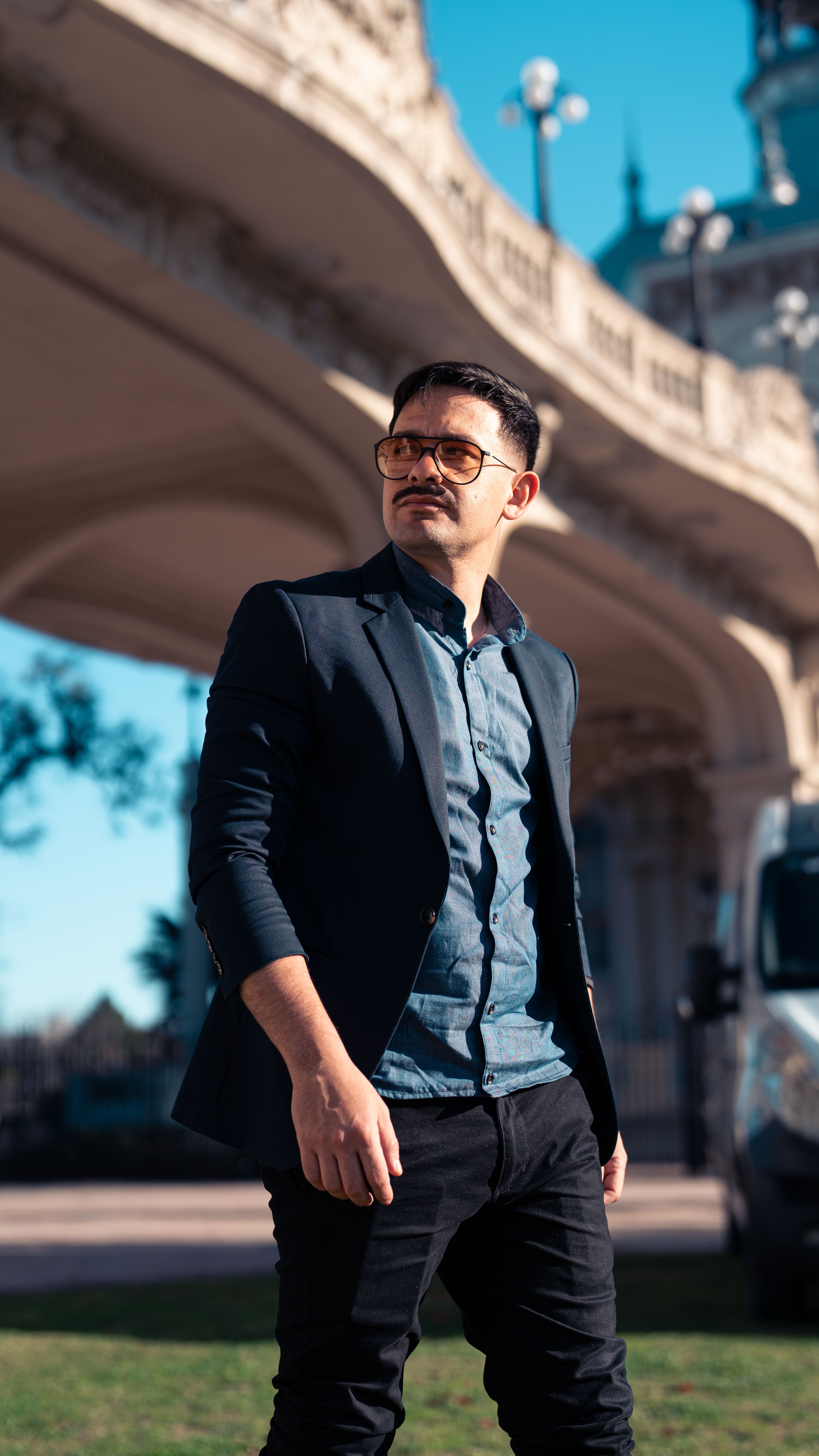 Man in a fashionable suit standing confidently under an elegant architectural bridge.