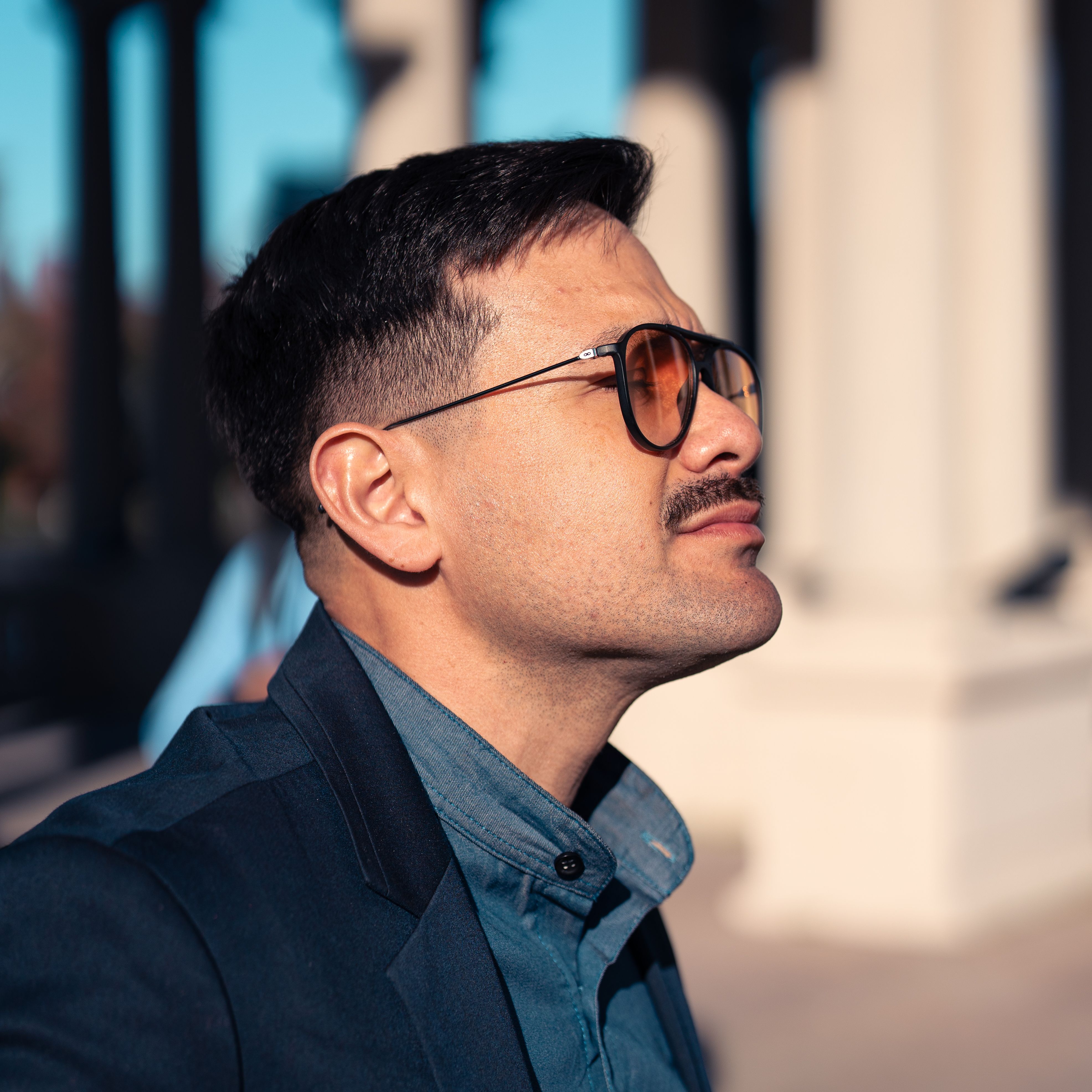 Profile of a stylish man wearing sunglasses, confidently posing outdoors in sunlight.