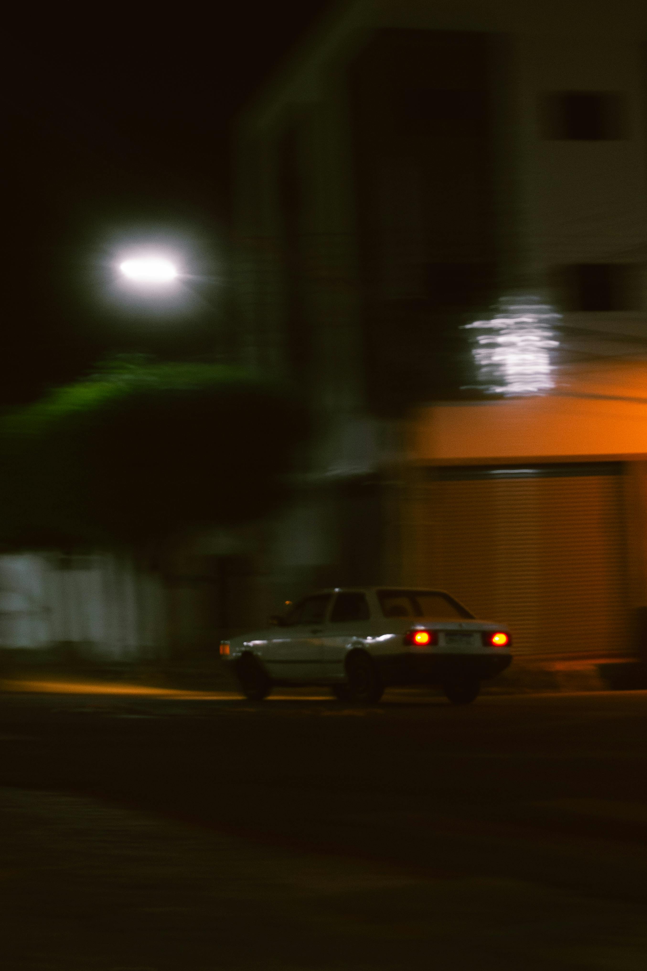 免费 老式汽车在夜间路灯下行驶的模糊运动照片，营造出忧郁的城市氛围。 素材图片