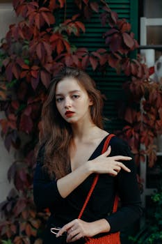 一位时尚女士以秋叶为背景，在户外摆出优雅的姿势，散发着现代时尚感