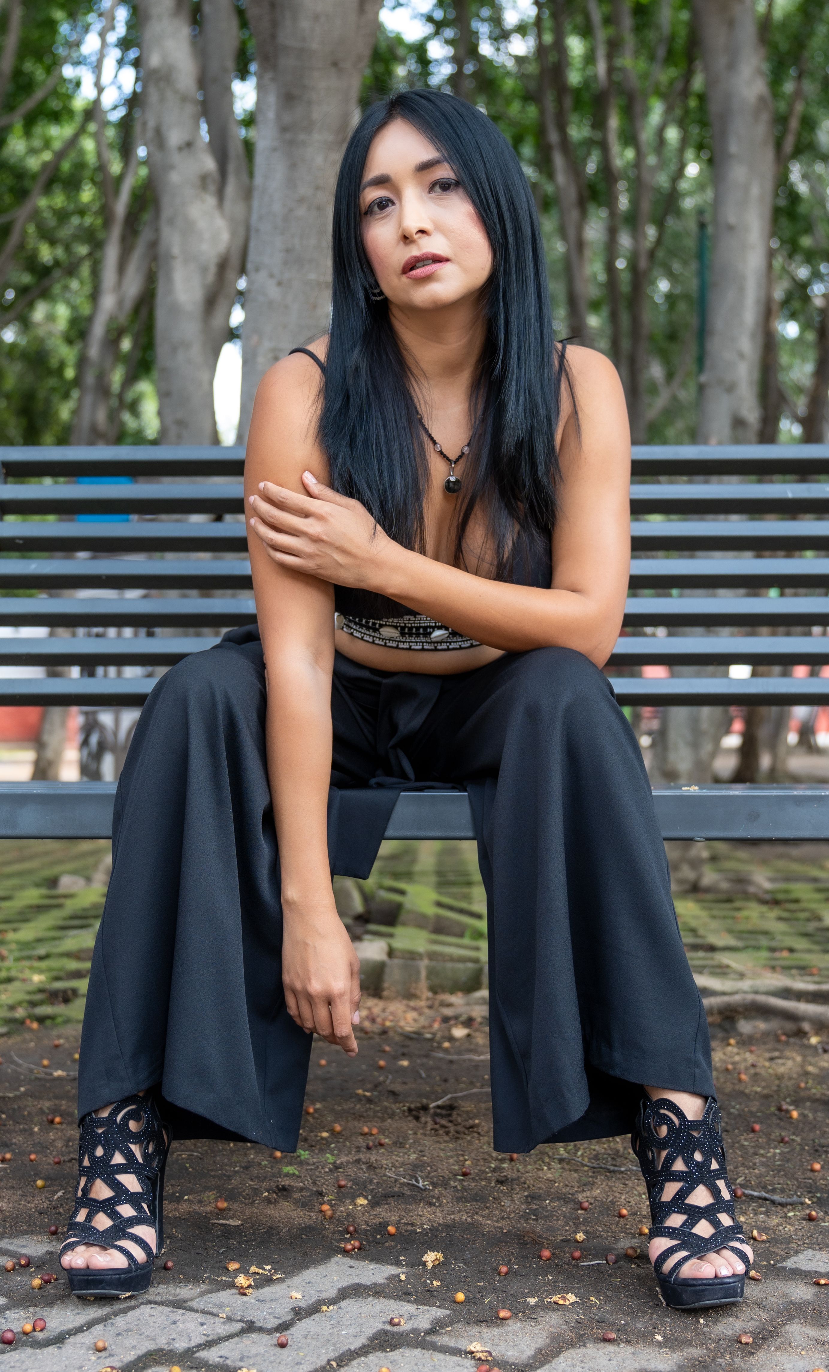 Fotomural Mujer con estilo sentada con confianza en un banco del parque en Ciudad de México, rodeada de árboles.