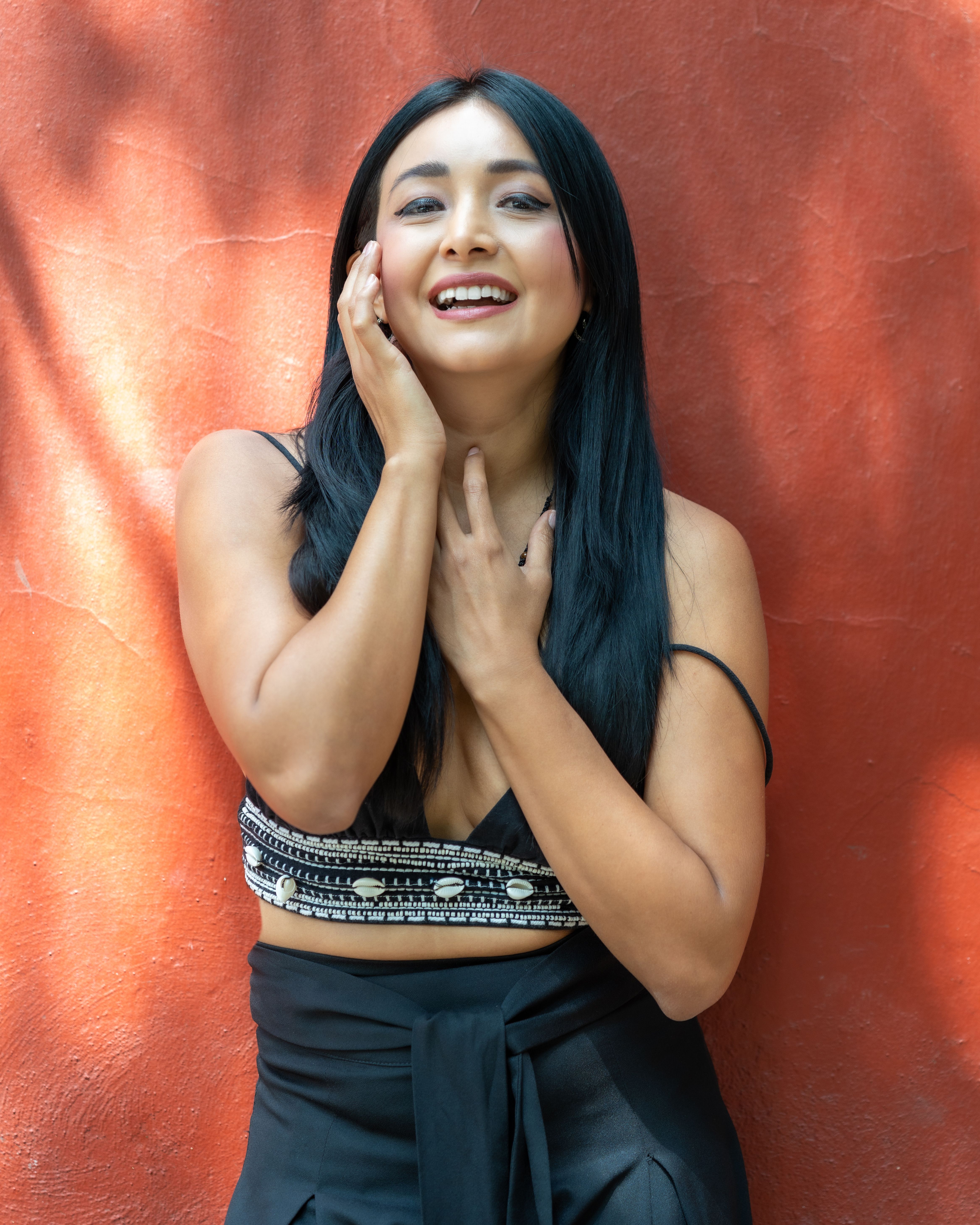 A cheerful woman posing with a vibrant smile against a red wall in Mexico City, CDMX.