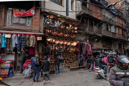 Market scene in Kathmandu with copperware, textiles, and local shoppers on a busy street.