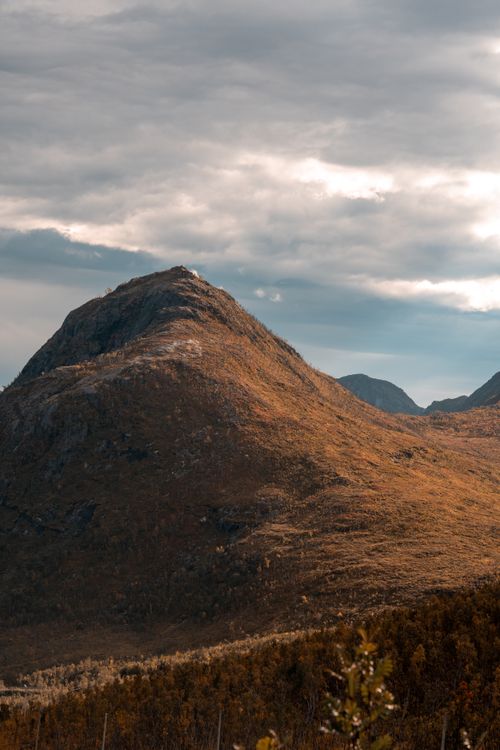Free Majestic mountain view in Tromsø, Norway, with warm autumn hues under a cloudy sky. Stock Photo
