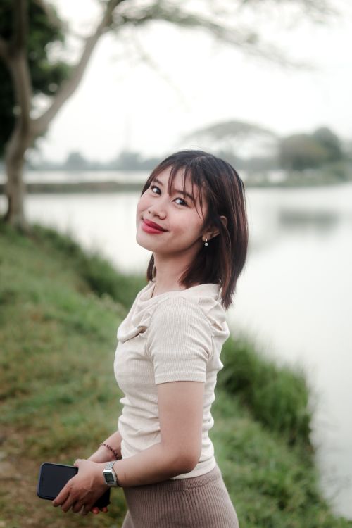 Free Young woman smiling while standing by a serene lake. Stock Photo