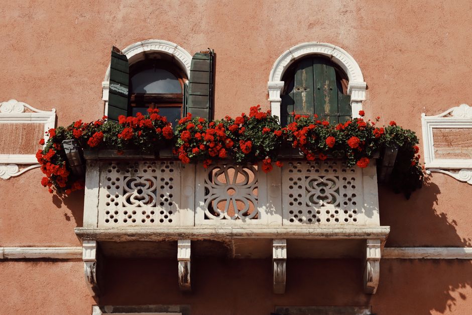Charming Venetian balcony adorned with vibrant red flowers in Venice, Italy.