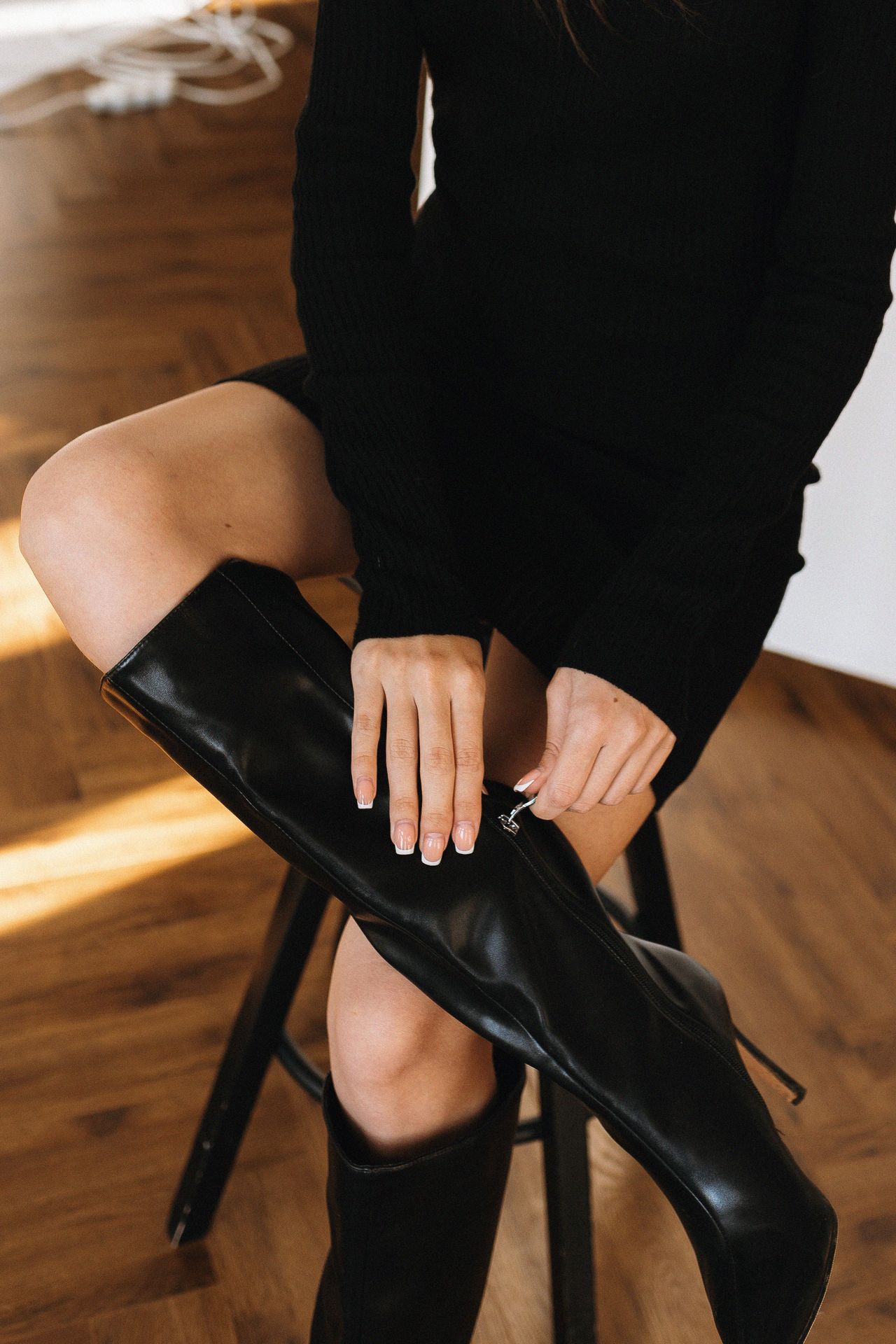 Woman zipping up a knee-high black leather boot indoors