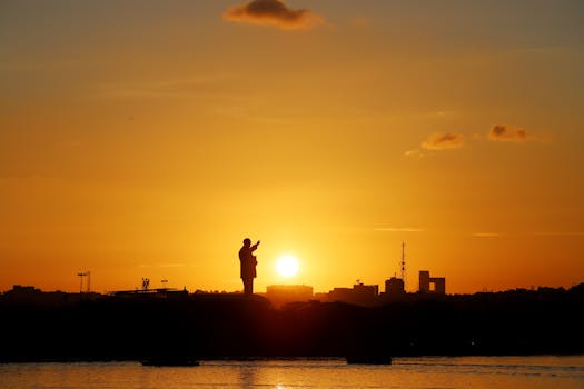 Silhouette of a statue against a stunning sunset backdrop, creating a dramatic cityscape scene.