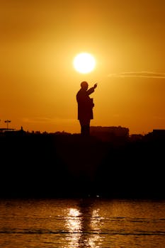 Silhouette of a person pointing at sunset over a calm sea, evoking a sense of mystery and reflection.
