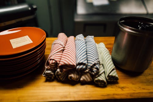 Rolled Assorted-colored Hand Towels Near Round Orange Ceramic Plates on Wooden Table