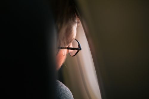 Free A thoughtful man gazing out an airplane window, wearing eyeglasses, in soft ambient lighting. Stock Photo