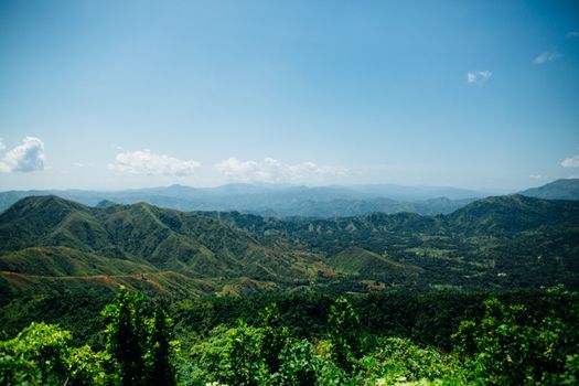 Expansive view of lush green hills and distant mountains under a clear blue sky.
