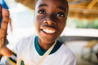 Child Wearing White and Green V-neck T-shirt Grinning