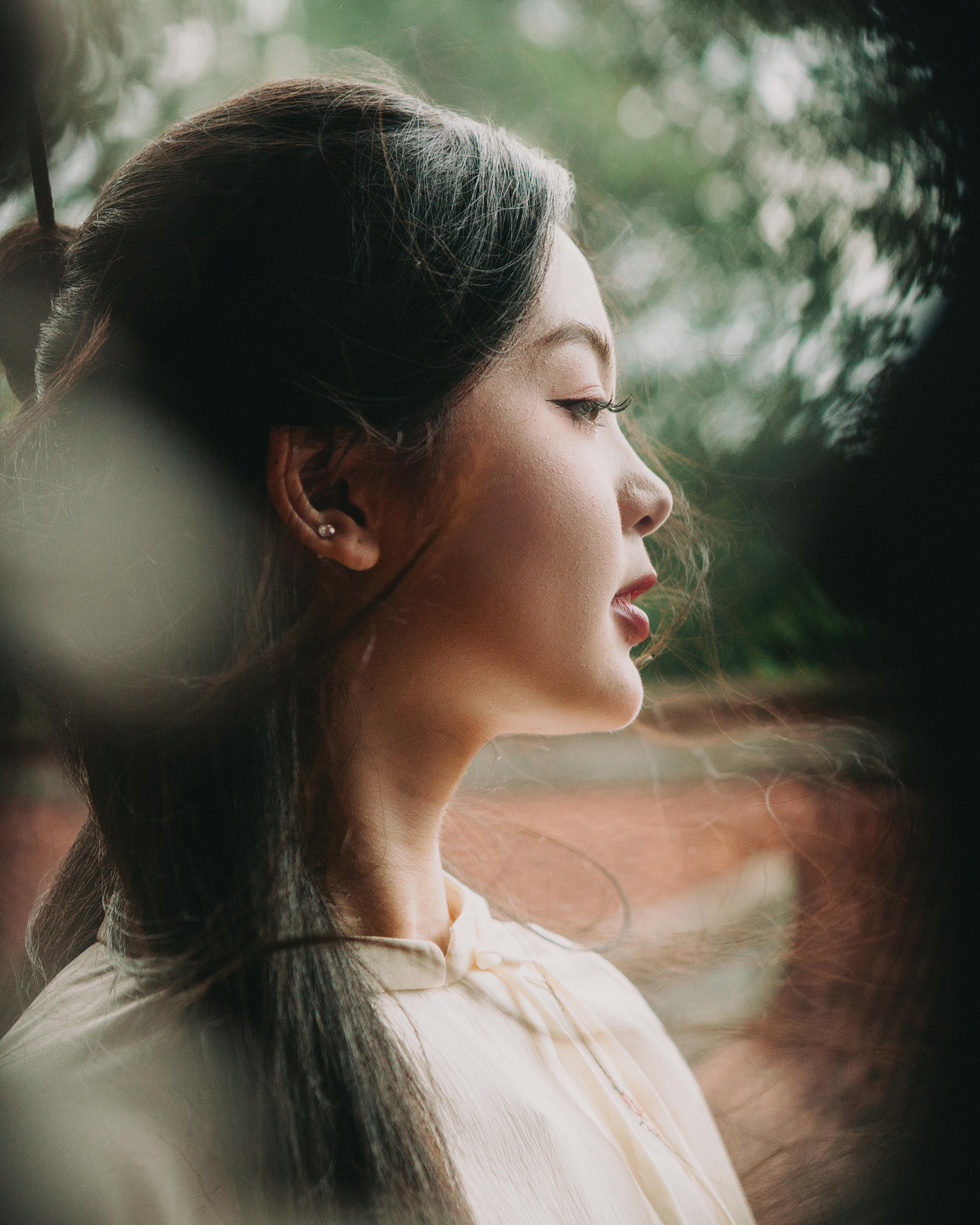Profile portrait of a woman in traditional Vietnamese Ao Dai amidst lush greenery.