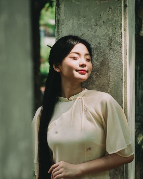 Free Portrait of a woman in traditional Ao Dai enjoying sunlight in Hà Nội, Vietnam. Stock Photo