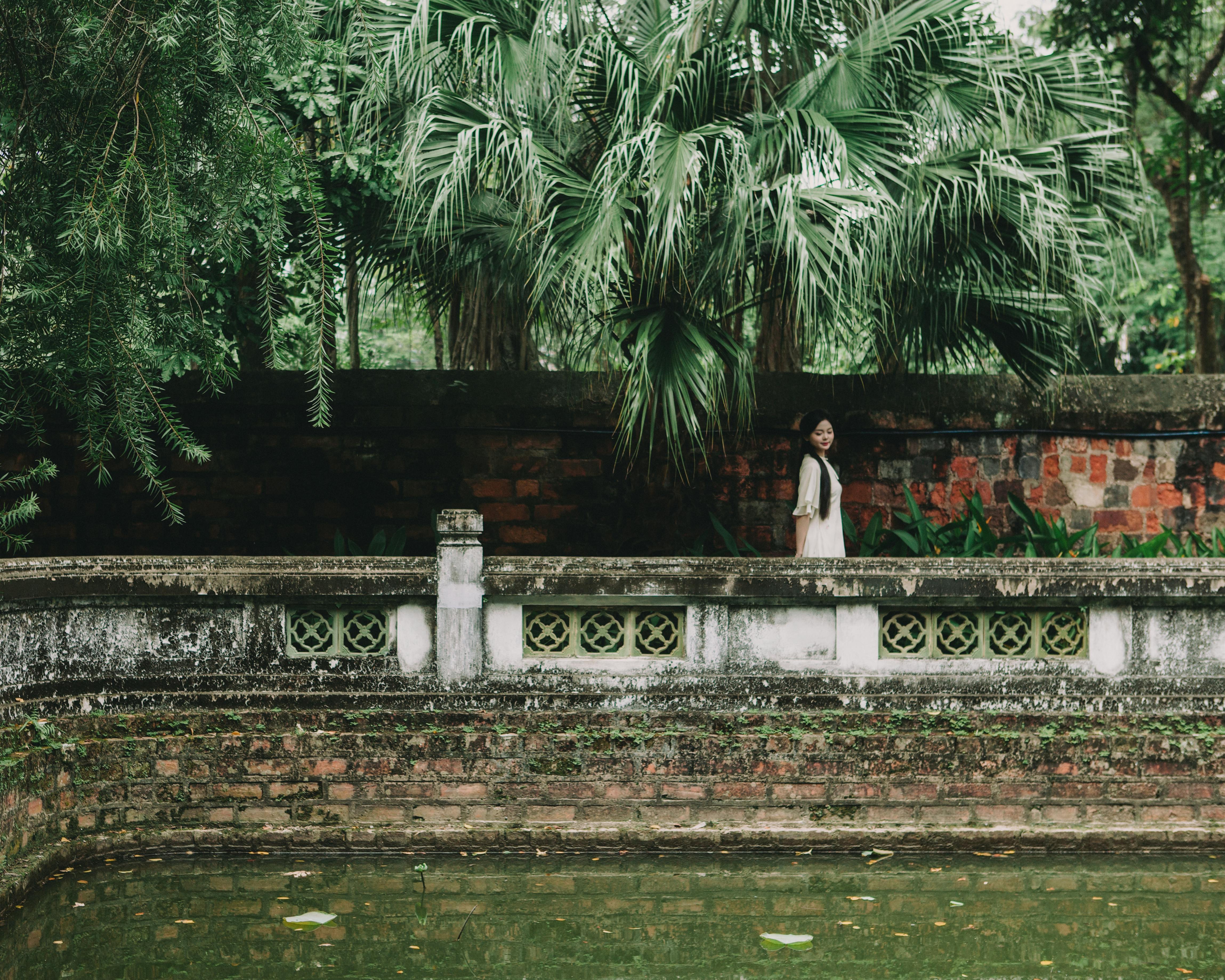 Woman in ao dai in lush garden at the Temple of Literature, Hanoi.