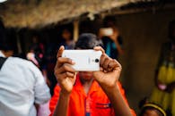 在拥挤的户外环境中，一个穿着鲜艳衣服的人正用智能手机自拍