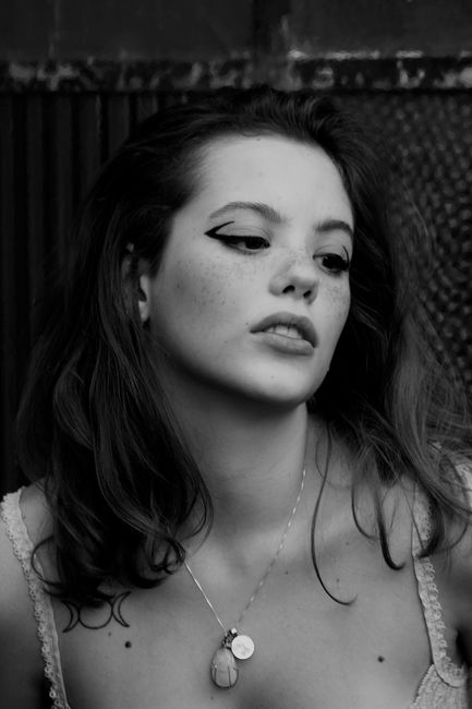 Artistic black and white portrait featuring a young woman with striking eyeliner and necklace.