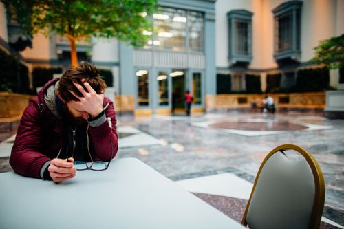 Free Man holding eyeglasses in hand, showing stress in a modern indoor atrium. Stock Photo