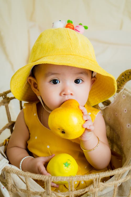 Bambino In Cima Gialla E Cappello Che Tiene Frutta