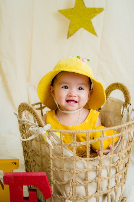 A cute baby in bright yellow attire smiling in a wicker basket with a star backdrop.