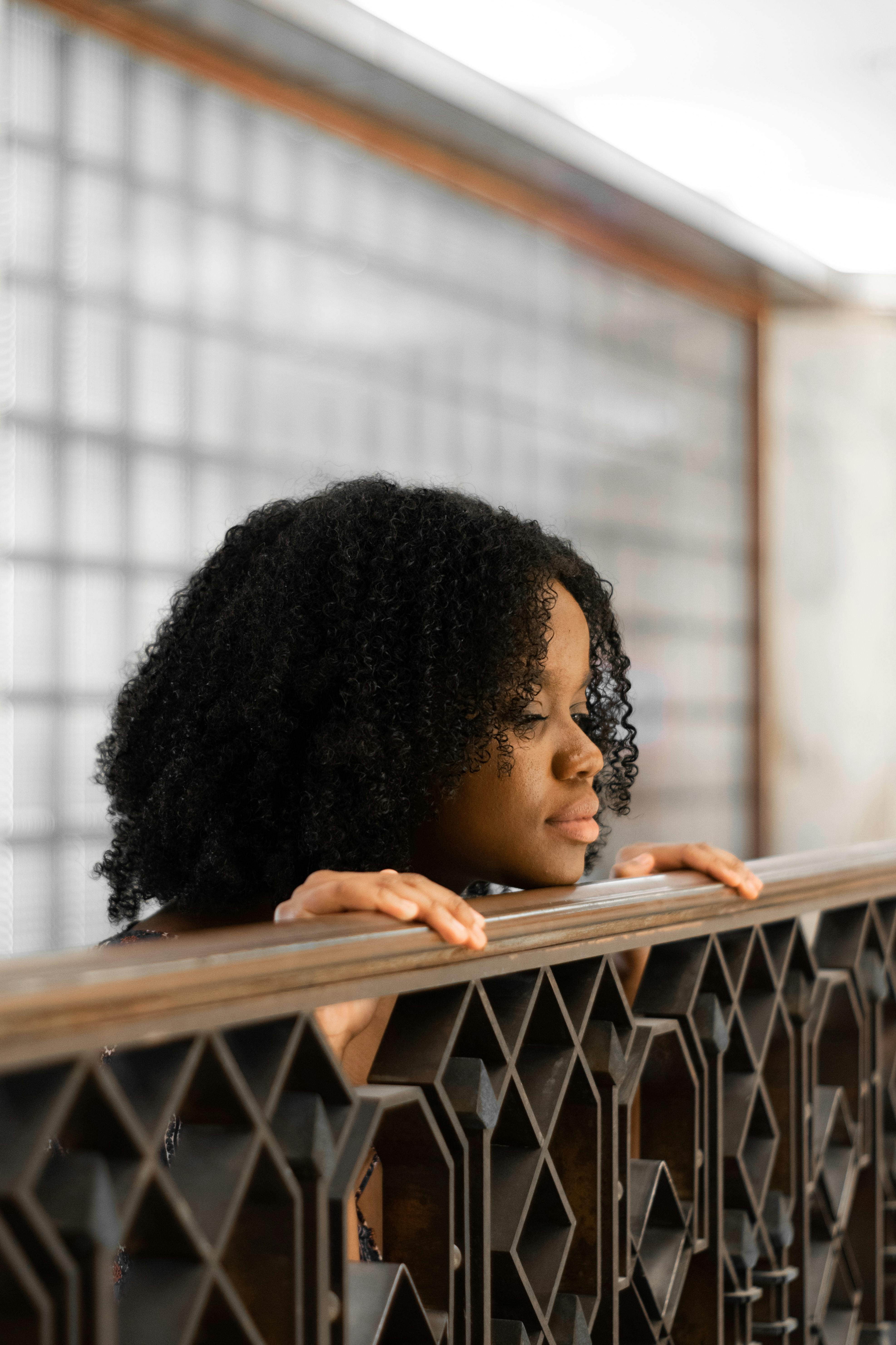一位卷发的女人若有所思地靠在室内，目光移向别处