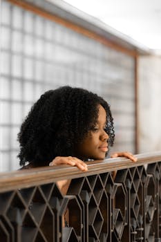 一位卷发的女人若有所思地靠在室内，目光移向别处