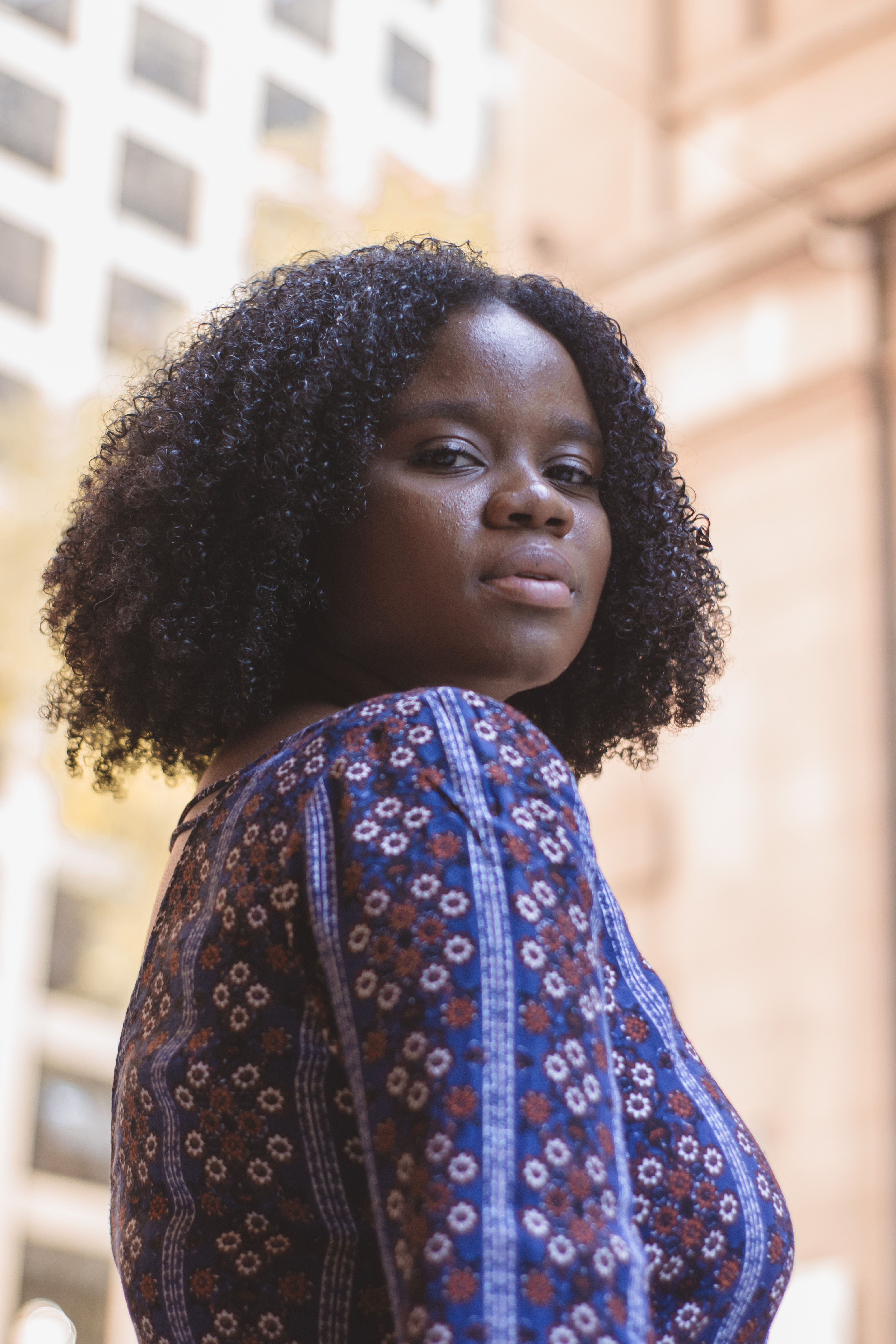 Elegant portrait of a woman with curly hair in a city environment, wearing a floral top.