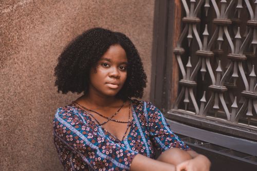 Free A woman with curly hair in casual wear sitting against a decorative window, captured during a photoshoot. Stock Photo