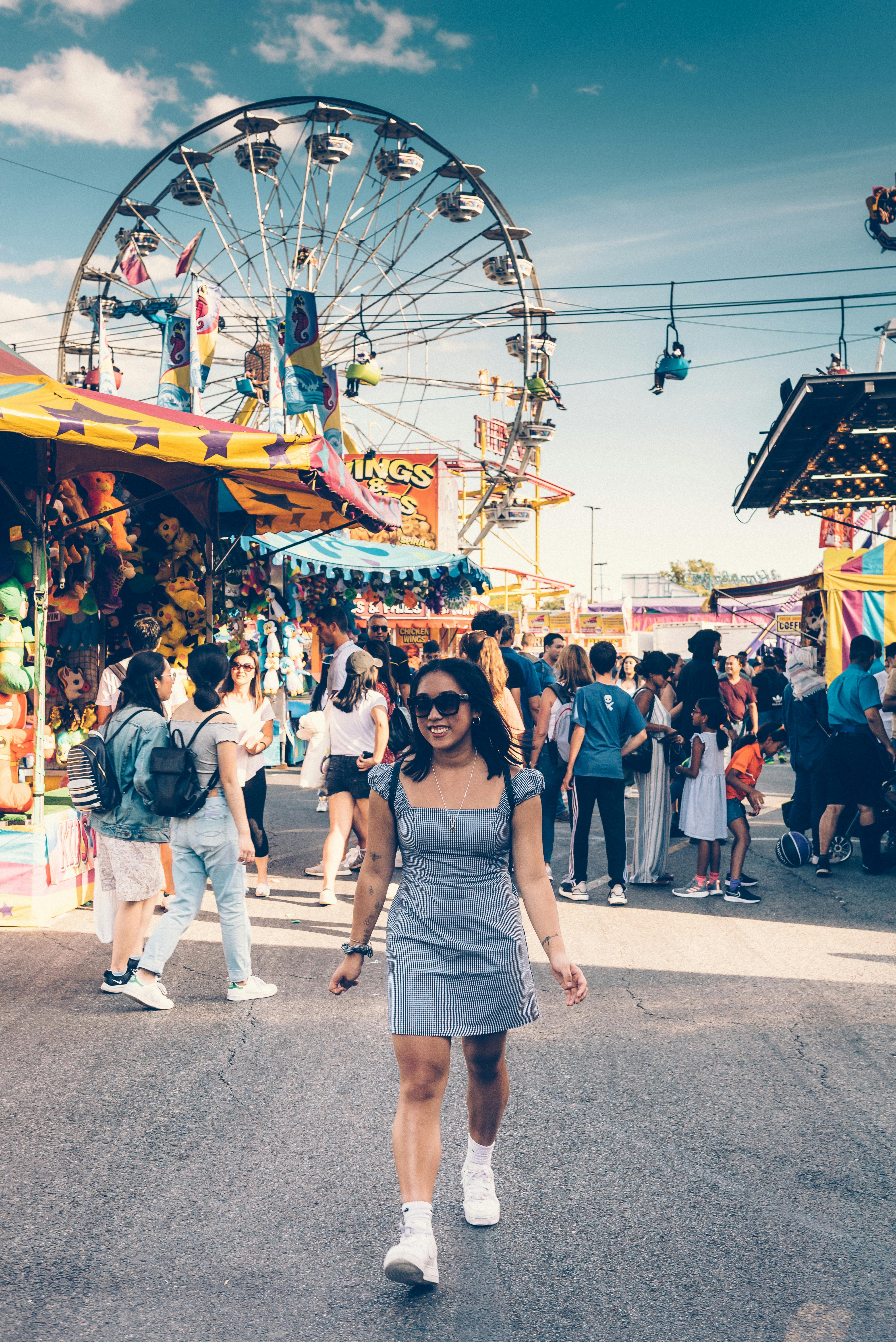 woman in gray square neck mini dress and white sneakers walking on street with ferris wheel background