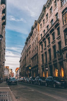 黄昏时分，一条繁忙的街道两旁，历史建筑与停放的汽车排列着