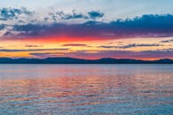 宁静的水面上，日落景色令人惊叹，色彩鲜艳，倒影熠熠生辉