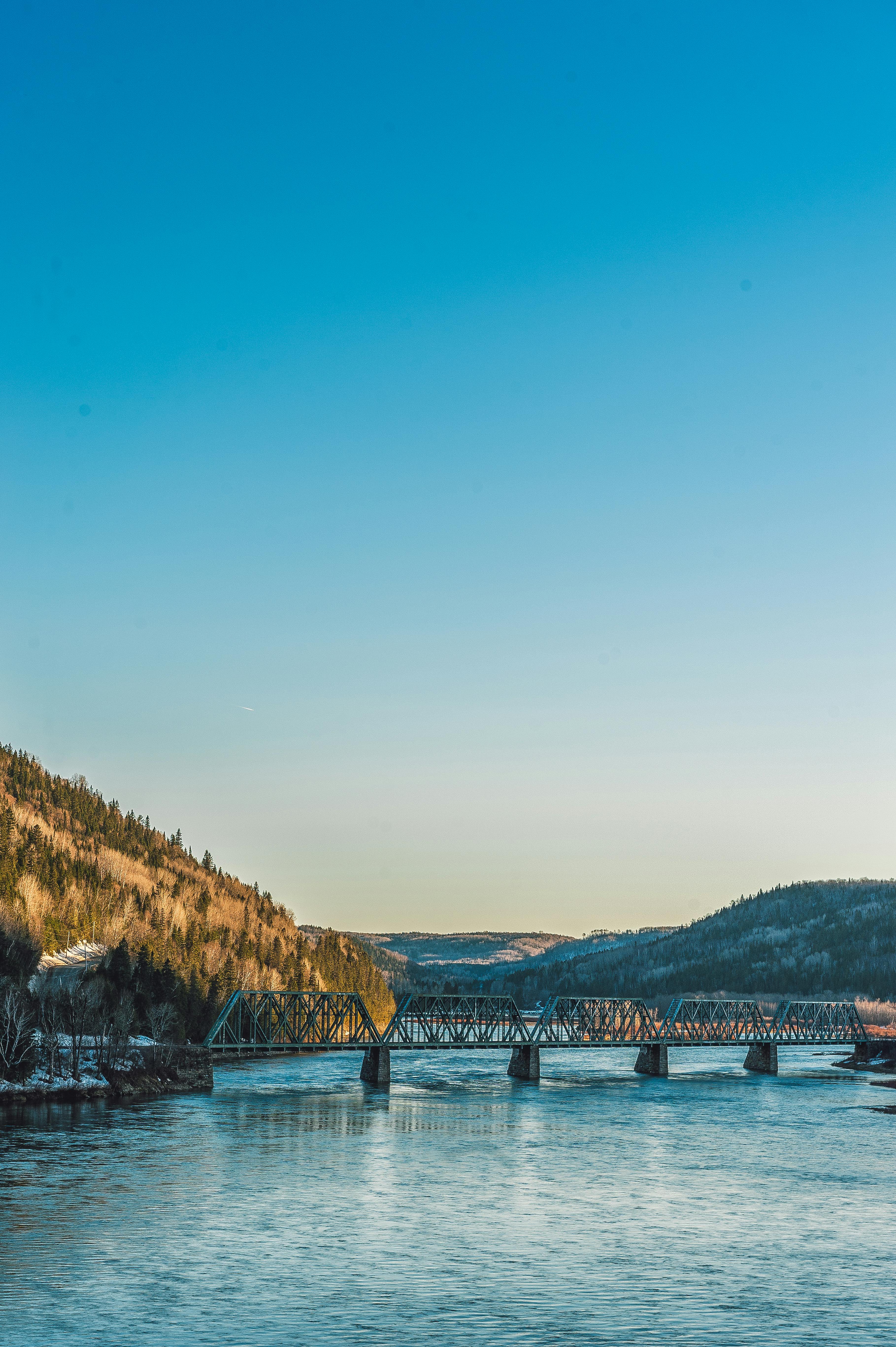 一座桥横跨河流，背景是蓝天下的山峦，景色令人惊叹