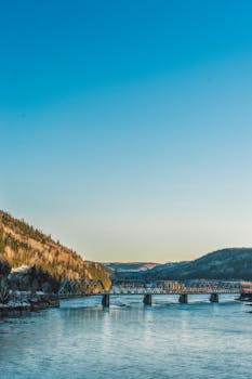 一座桥横跨河流，背景是蓝天下的山峦，景色令人惊叹