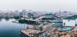 海边一个雾气缭绕的宁静村庄，展示着船只、码头和乡村房屋