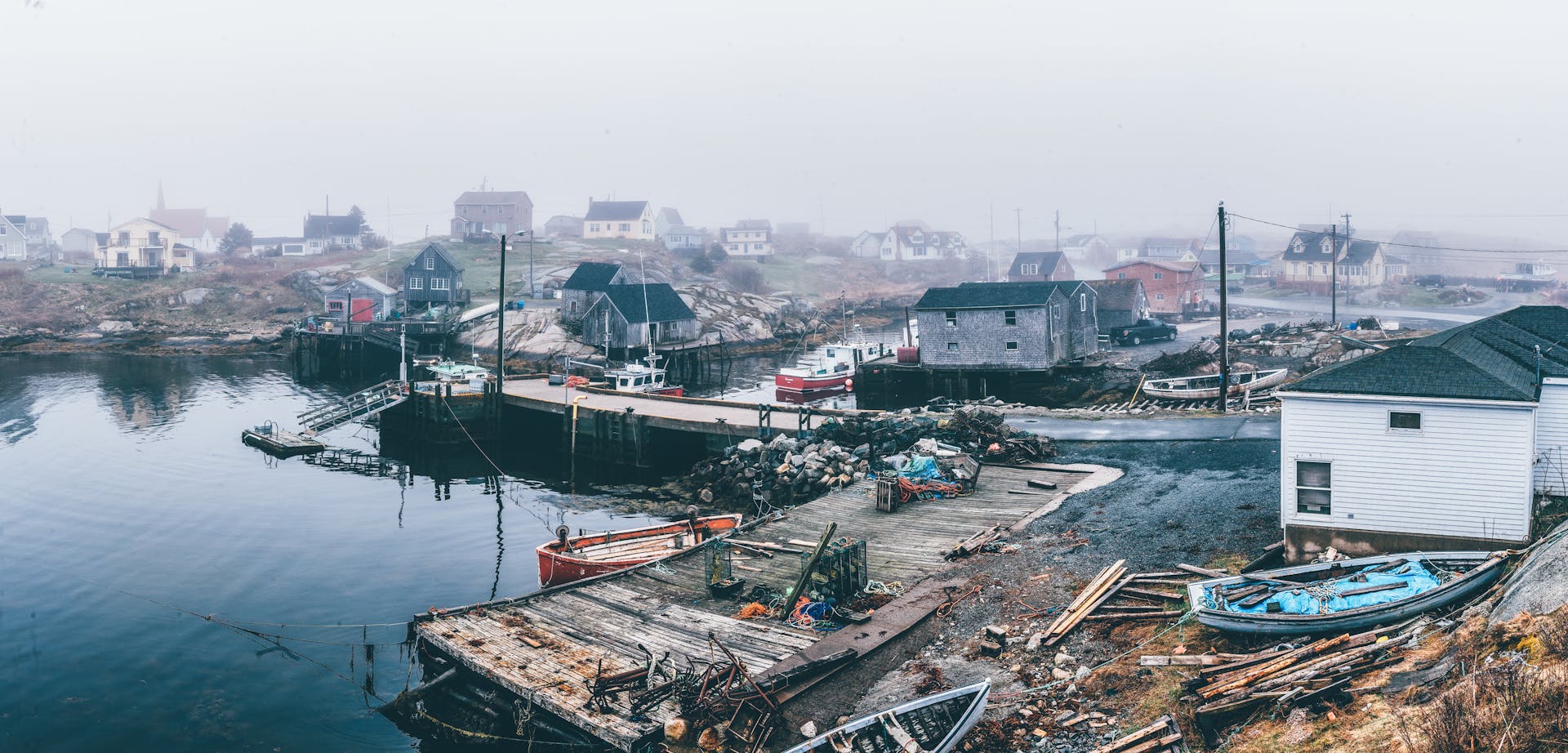 A serene foggy village by the sea, showcasing boats, marina, and rustic houses.