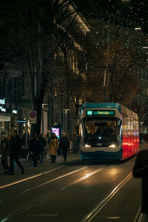 Free A tram travels through a bustling city street at night with festive lights overhead. Stock Photo
