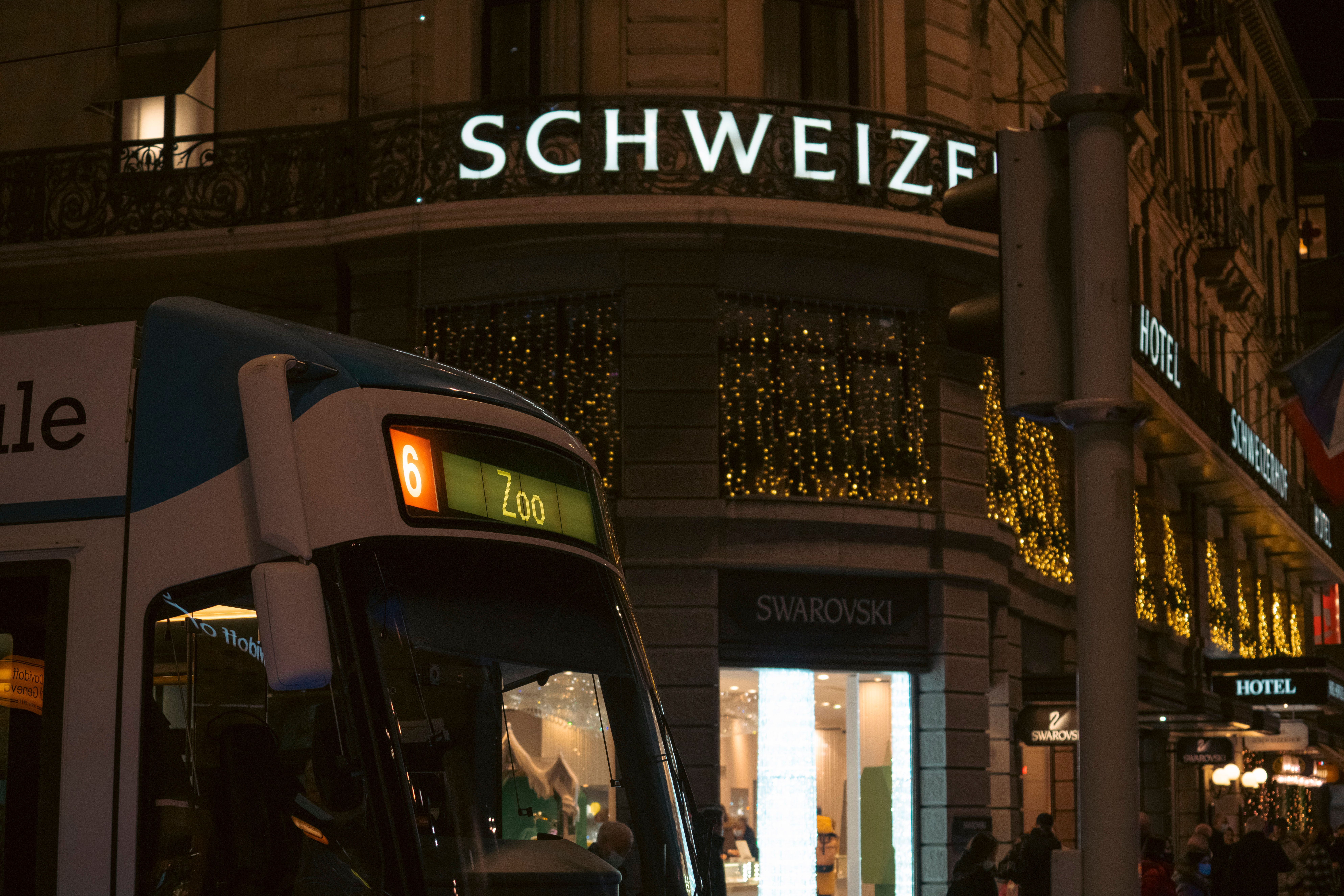 Urban evening scene with a tram passing by illuminated shops in a bustling city center.