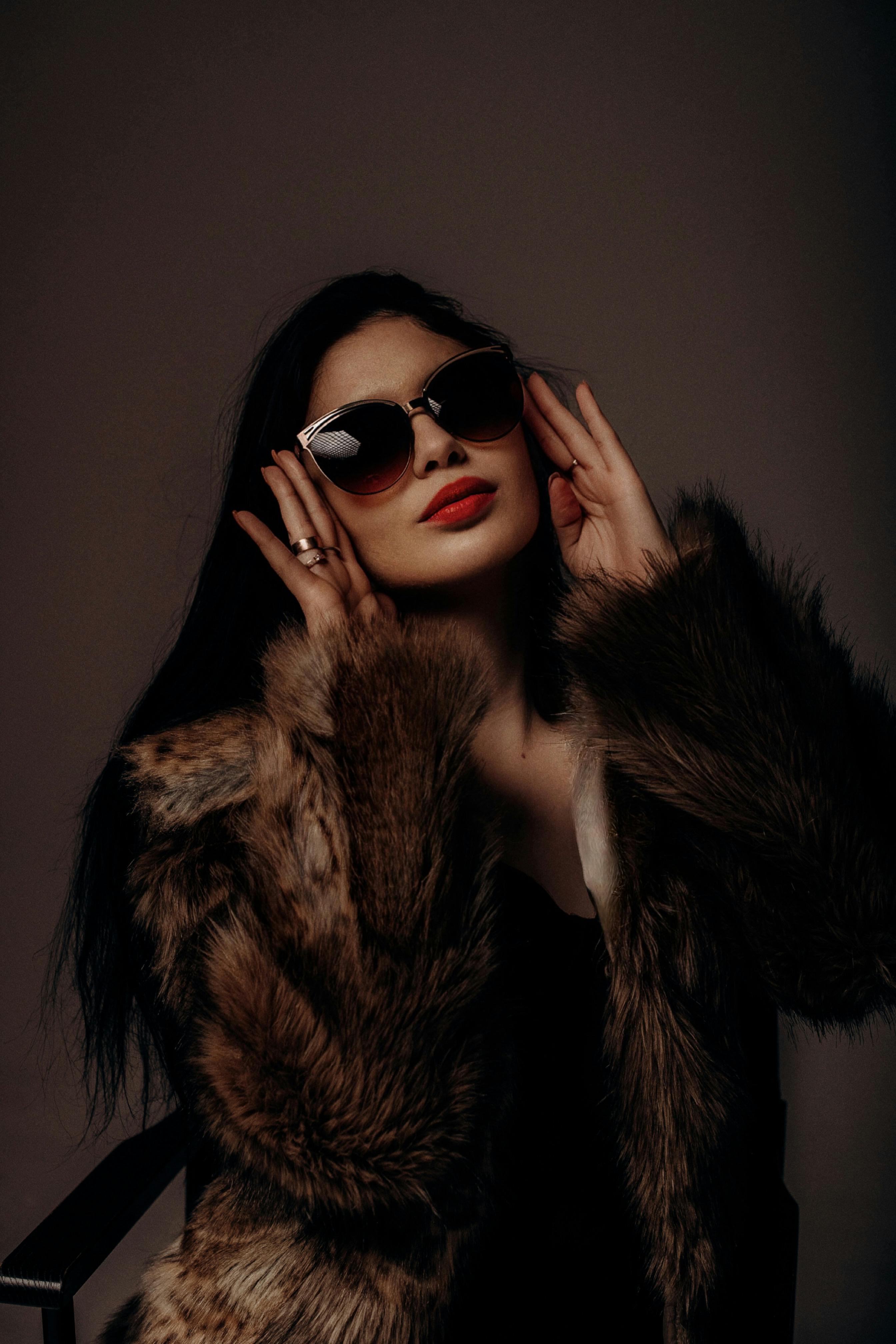 Free Elegant woman posing in fur coat with sunglasses on dark background. Stock Photo